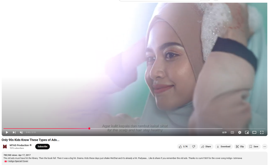 Screenshot from a YouTube video titled ‘Only 90s Kids Know These Types of Ads…’ uploaded by MTAS Production, showing a Malaysian Muslim woman smiling while gently applying shampoo foam over her hijab. The woman wears a beige headscarf, and the scene is brightly lit, symbolizing freshness. The video has over 780,000 views and was published on April 17, 2017. English subtitles at the bottom translate the Malay text as ‘for the scalp and hair stay healthy.’ The ad has drawn attention online with questions about why the woman is shampooing her hijab, sparking debates and misunderstandings, though the commercial is metaphorical and respects cultural values. The video reflects nostalgic content with the tagline ‘Only 90s Kids Know,’ combining traditional advertising styles with contemporary representation.